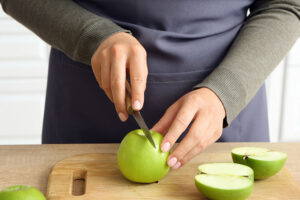 Cerca de manos cortando manzanas verdes por la mitad en una tabla para cortar