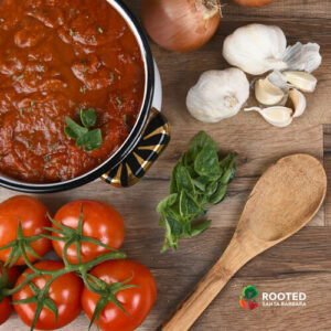 Tomatos, onions and garlic next to a pot of simmering tomato sauce