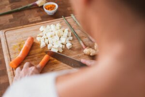 Looking over a woman's shoulders as she chops carrots and onions