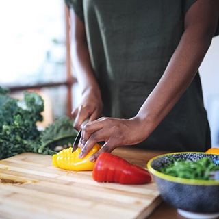 Preparando sus verduras: dos manos cortan pimientos amarillos y rojos en una tabla para cortar