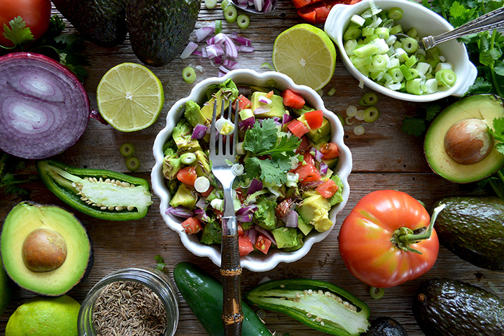 Fotografía cenital de una ensalada recién hecha en un recipiente con borde estriado, rodeada de vegetales coloridos