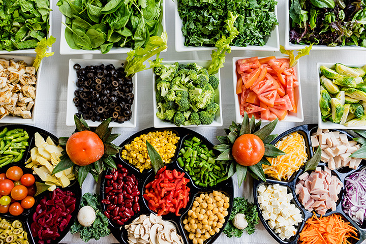 Overhead shot of two pair of hands preparing colorful fruits and vegetables on a kitchen cutting board