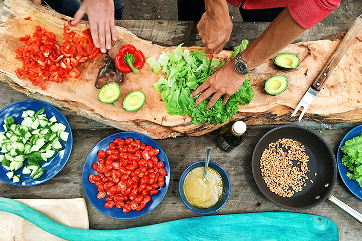 Overhead shot of two pair of hands preparing colorful fruits and vegetables on a kitchen cutting board