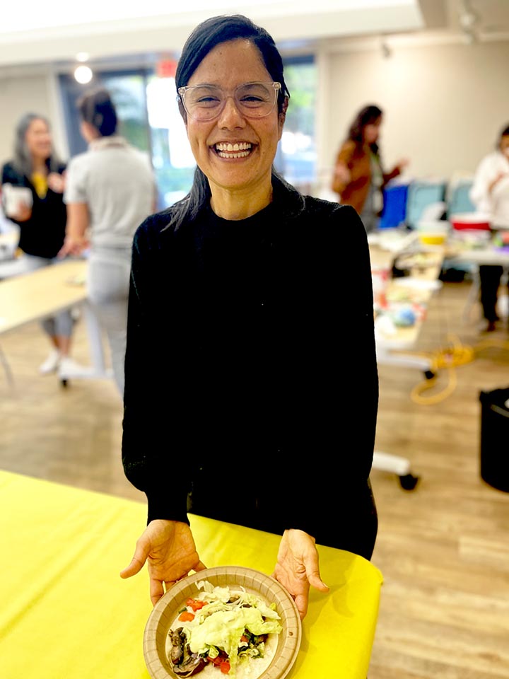 rsb-2025-064-9589-lib-clase-de-cocina Una mujer sonriente que asiste a una clase de cocina sonríe y sostiene un plato brillante de comida preparada.
